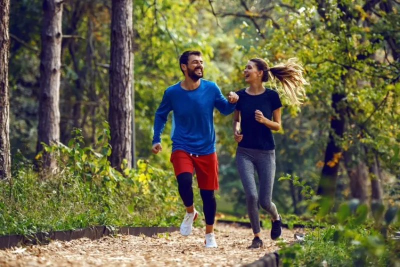 full length of fit sporty happy caucasian couple in sportswear running in woods on trail in morning