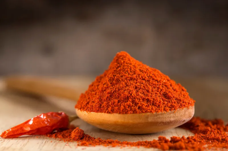 spoon filled with red hot paprika powder and red hot chili pepper over wooden background