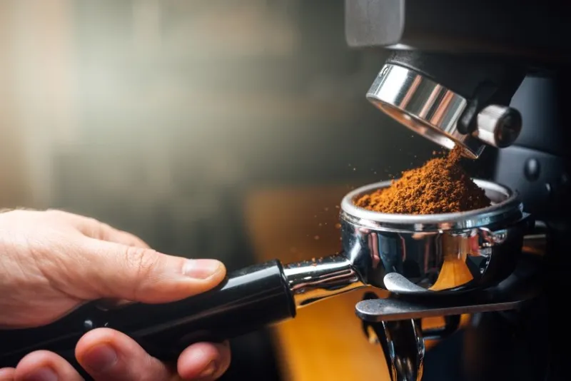 ground coffee pouring into a portafilter with a grinder, closeup