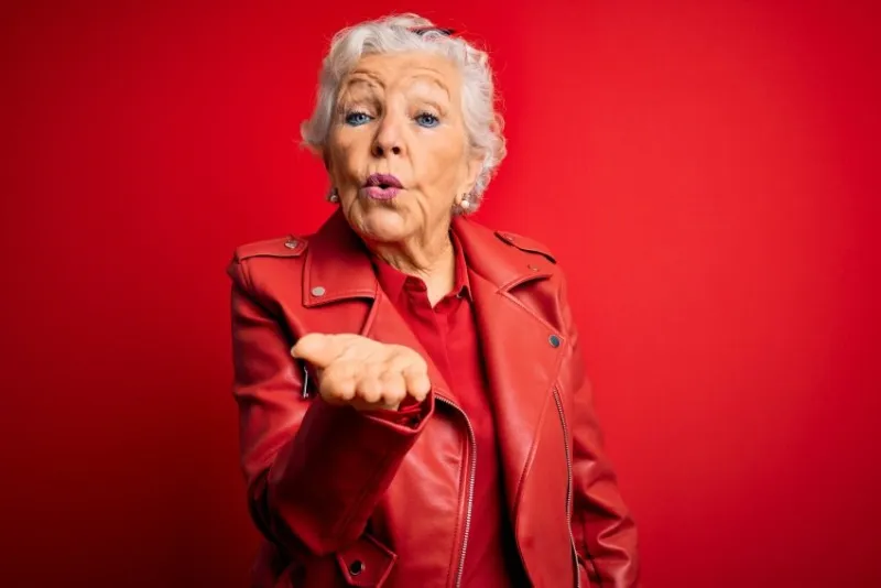 senior beautiful grey-haired woman wearing casual red jacket and sunglasses looking at the camera blowing a kiss with hand on air being lovely and sexy love expression