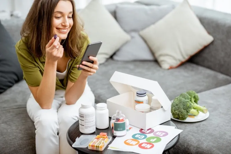 woman taking nutritional supplements in the form of pills while sitting with smart phone at home concept of individual online selection of food supplements preventive medicine