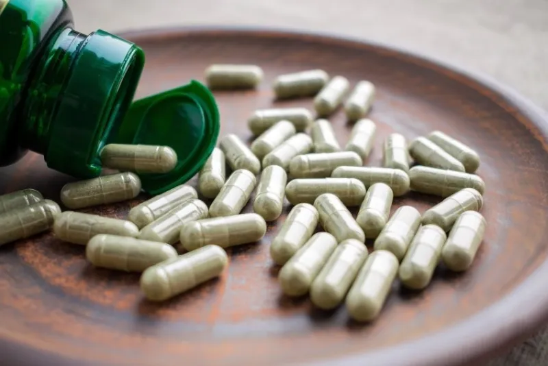 close up green tea extract capsules and bottle on a clay brown plate on a burlap background dietary supplements, vitamins, minerals, vegans, vegetarians healthy lifestyle, superfood selective focus