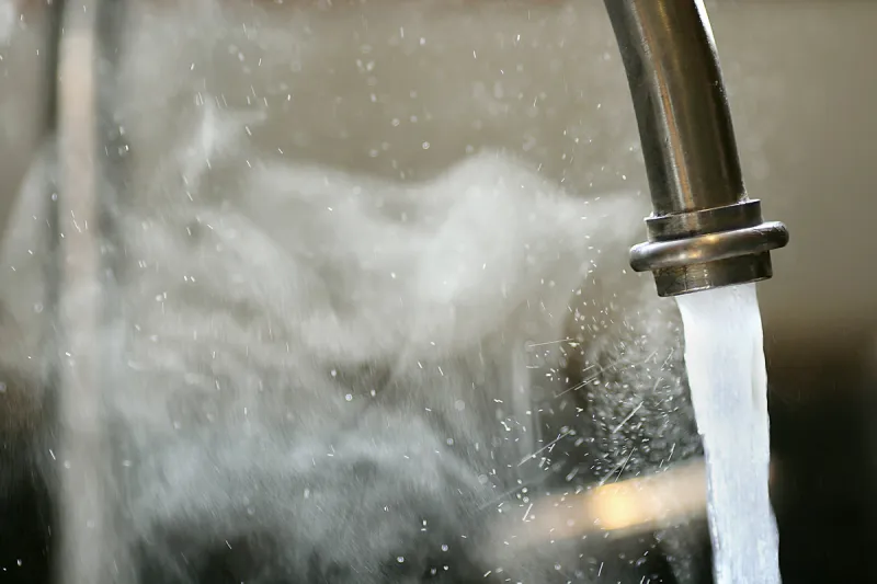 hot steaming running tap water is pouring out of a stainless steel kitchen faucet