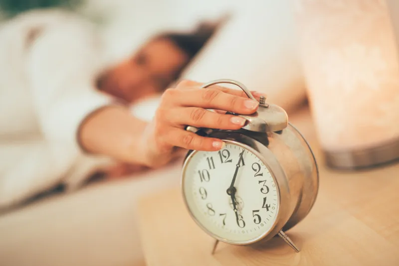 beautiful young woman sleeping in bed and holding hand on alarm clock selective focus focus on foreground, on clock
