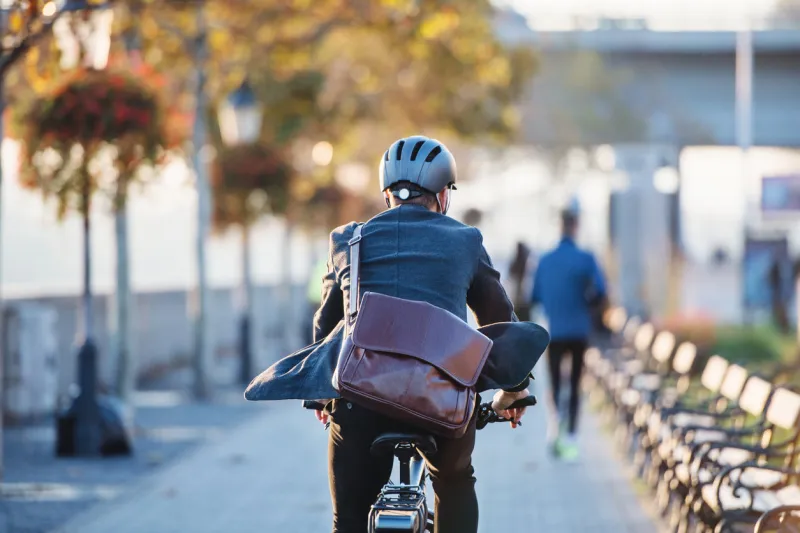 a rear view of a businessman commuter with electric bicycle traveling to work in city copy space