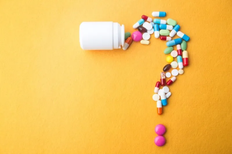 pills or capsules as a question mark and white plastic bottle