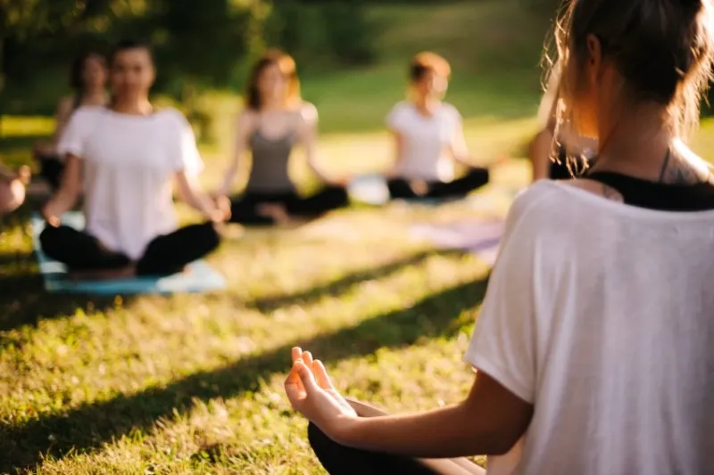group of young sporty woman practicing yoga lesson with instructor, sitting in lotus pose focus of camera at teacher rear view photo from back of instructor group of meditating people in background