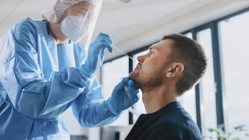 medical nurse in safety gloves and mask, protective face shield and overalls is taking a pcr corona virus sample in a health clinic doctor uses respiratory swab test covid-19 pandemic concept