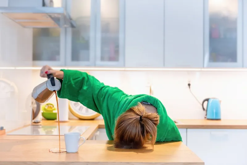 tired woman sleeping on the table in the kitchen at breakfast trying to drink morning coffee