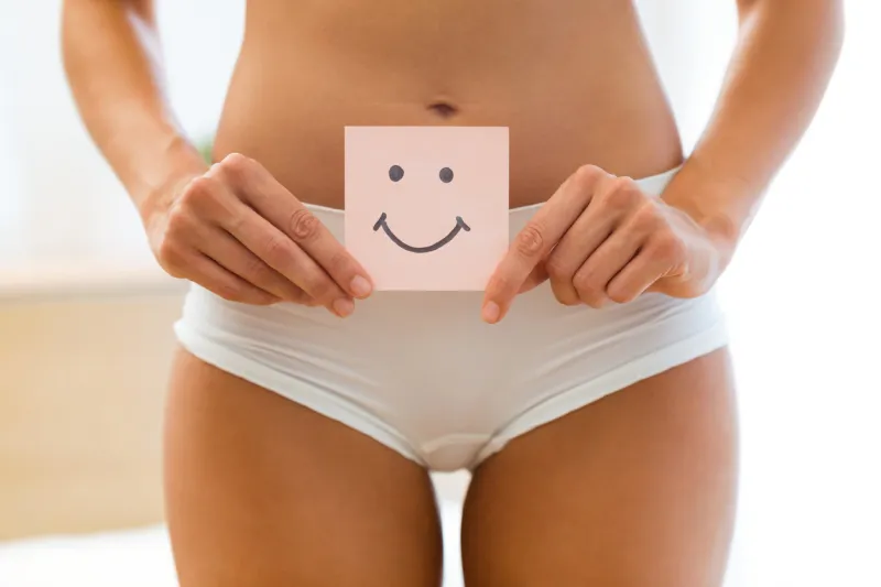 close-up of young woman holding paper with smile mark over her stomach health hygiene sexual education concept