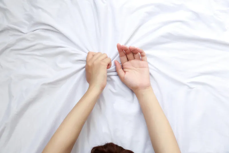 close up woman hands grasping the blanket in the moment of sexual pleasure or orgasm ecstasy sex creator concept