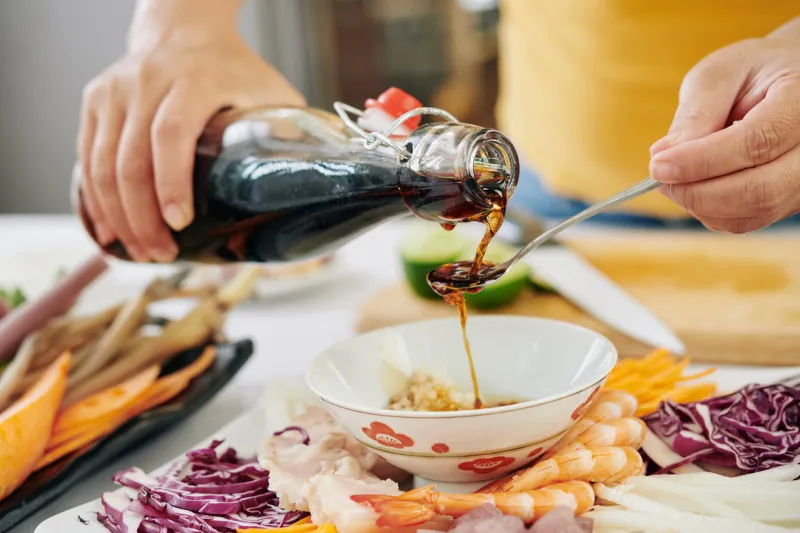woman pouring couple of tea spoons of soy sauce into small bowl when making dipping sauce for snack plate