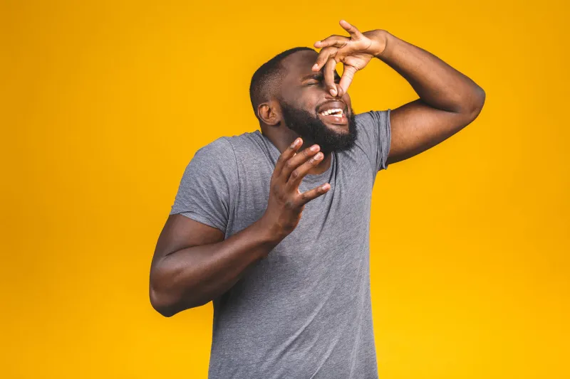 afro american man isolated against yellow background smelling something stinky and disgusting, intolerable smell, holding breath with fingers on nose bad smells concept