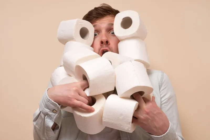 young sad caucasian man holding several roll of toilet paper deficit in shops because of coronavirus panic