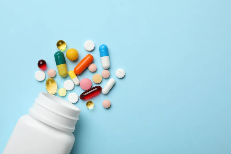 bottle and scattered pills on color background, top view space for text