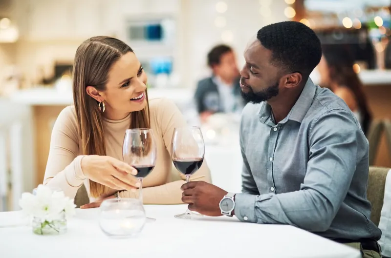 love, wine and interracial couple on date for fine dining, restaurant or valentines celebration together black man and happy woman with romance alcohol glasses, celebrate and luxury in night bokeh
