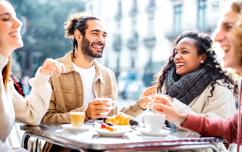 young couples drinking cappuccino at coffee bar patio - friends talking and having fun together at sidewalk cafeteria - life style concept with young men and women at cafe dehor - bright vivid filter