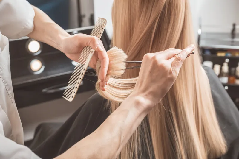 hairdresser is cutting long blond hair in hair salon