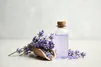 bottle of essential oil and lavender flowers on light stone table