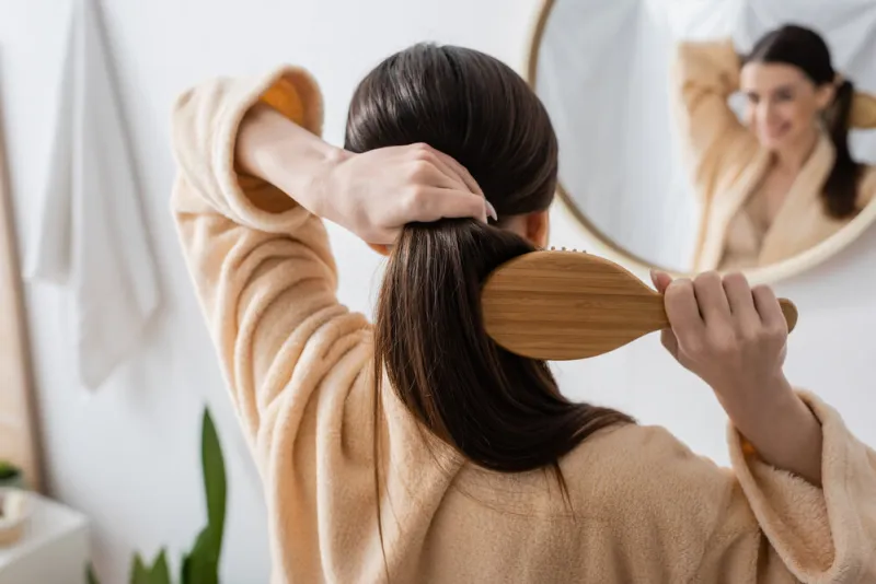 back view of young brunette woman brushing hair in bathroom,stock image