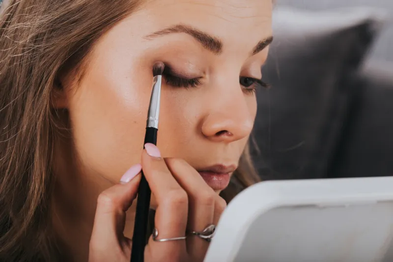 close up portrait of beautiful young woman applying eyeshadow powder with brush