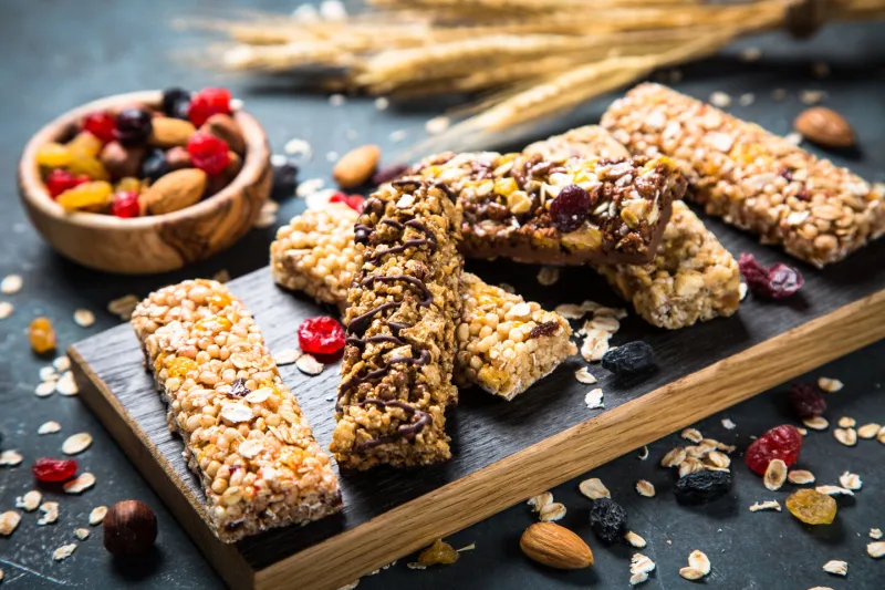granola bar with nuts, fruit and berries on cutting board at dark stone table