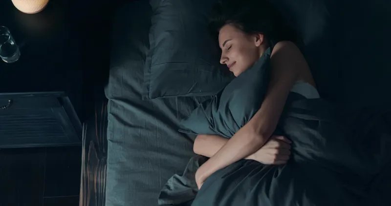 beautiful young brunette woman sleeping on side, lying cozily in bed, hugging a pillow lady sound asleep at night loft interior