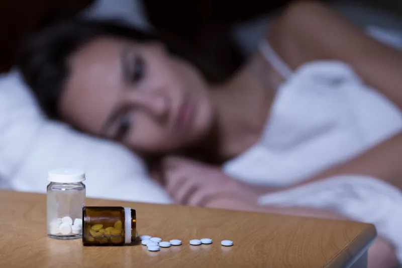 woman lying in bed, taking sleeping pills