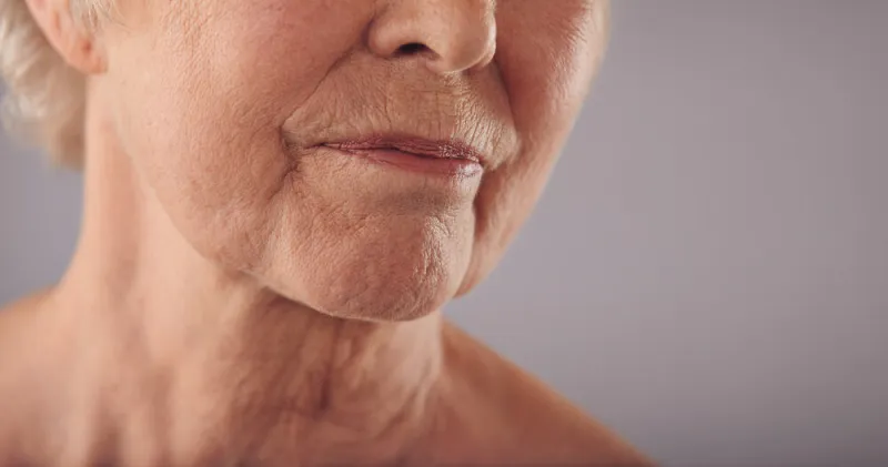 macro of a senior female face with wrinkled skin against grey background cropped old woman face