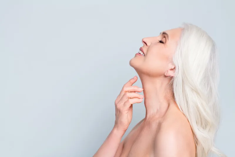 close-up profile side view portrait of attractive dreamy cheery grey-haired elderly lady touching soft skin neck isolated gray pastel color background