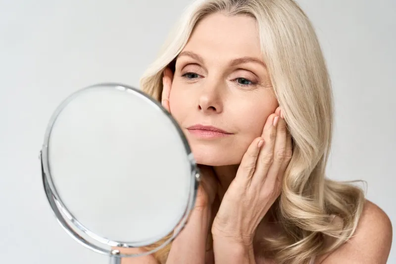 closeup portrait of gorgeous happy middle age woman looking at mirror touching her skin enjoying treatment for dry skin advertising of antiaging beauty skin care products