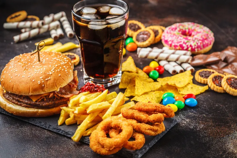 junk food concept unhealthy food background fast food and sugar burger, sweets, chips, chocolate, donuts, soda on a dark background