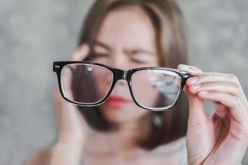 asian woman holding eyeglasses having headache from eye blur vision