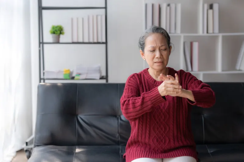 asian old woman with body aches, leg pain, bone pain, stiff muscles, arm pain, hand pain, sitting on the sofa in the living room stretching to relax