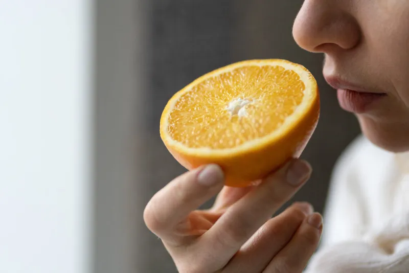 sick woman trying to sense smell of half fresh orange, has symp