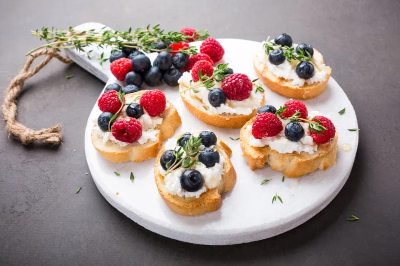 sandwiches with fresh berries, goat cheese and honey on marble cutting board, copy space