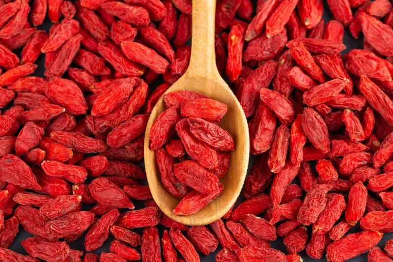 spoon with goji berries over red goji background healthy food concept