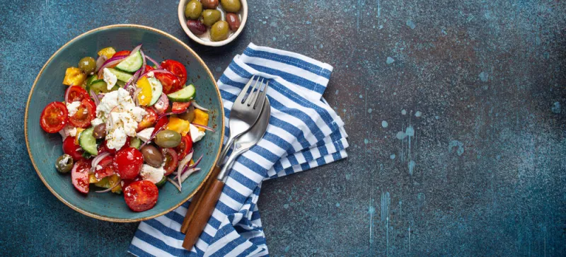 greek fresh healthy colorful salad with feta cheese, vegetables, olives in blue ceramic bowl on rustic concrete background top view, mediterranean diet, traditional cuisine of greece space for text