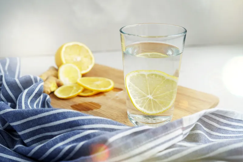 refreshing drink with lemon on a gray background warm water with a slice of lemon next to a blue napkin glass on a wooden board