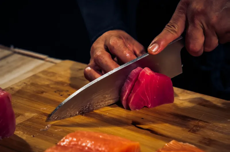 close up of chef cook hands chopping tuna fish for traditional asian cuisine with japanese knife professional sushi chef cutting seafood japanese chefs are making tuna fish sashimi dark tone