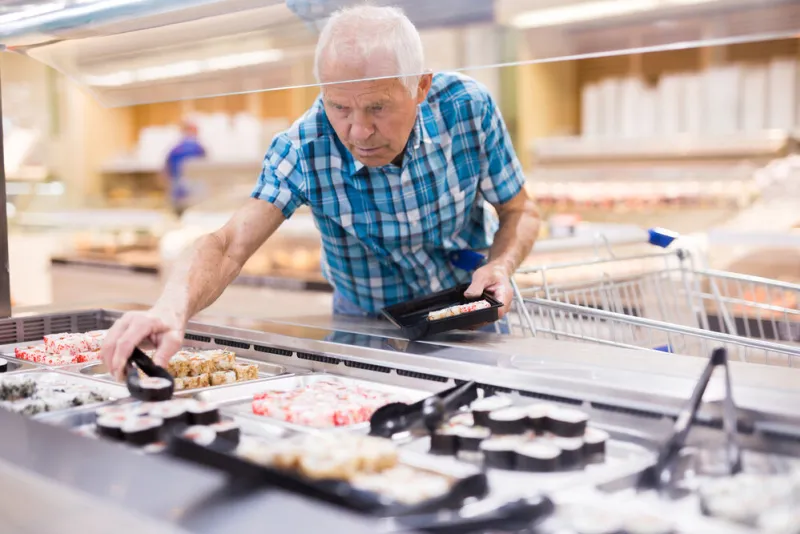 elderly retired senor buying sushi in buffet department of super
