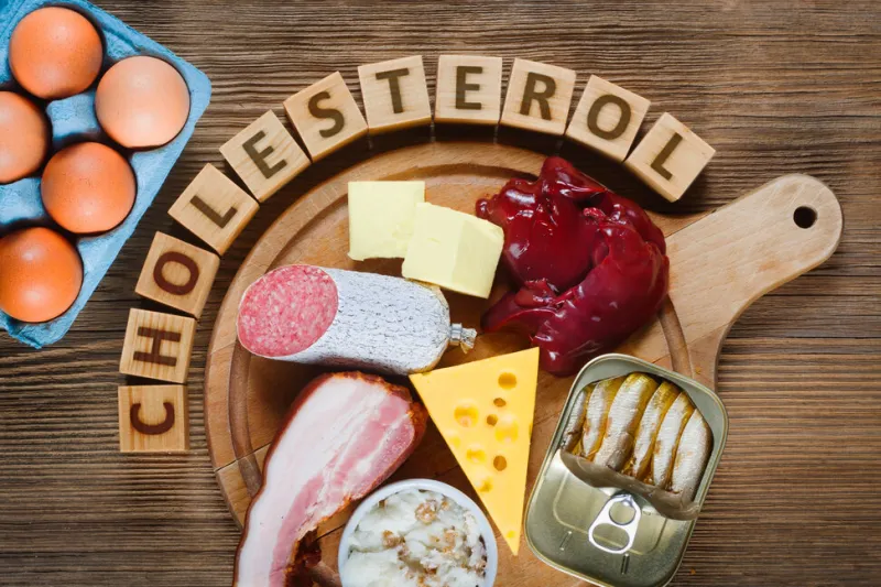 high-cholesterol foods as eggs, liver, yellow cheese, butter, bacon, lard with onion, sardines in oil wooden table as background