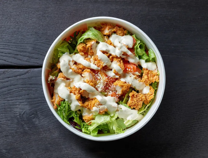 take away bowl of caesar salad with sauce on black wooden table, top view