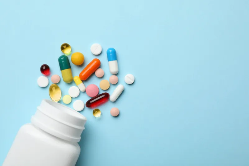 bottle and scattered pills on color background, top view space for text