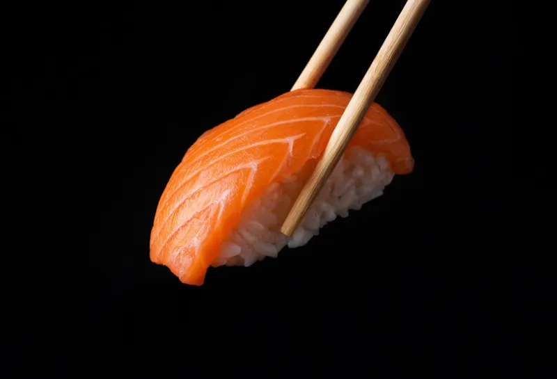 traditional japanese nigiri sushi with salmon placed between chopsticks, separated on black background side view