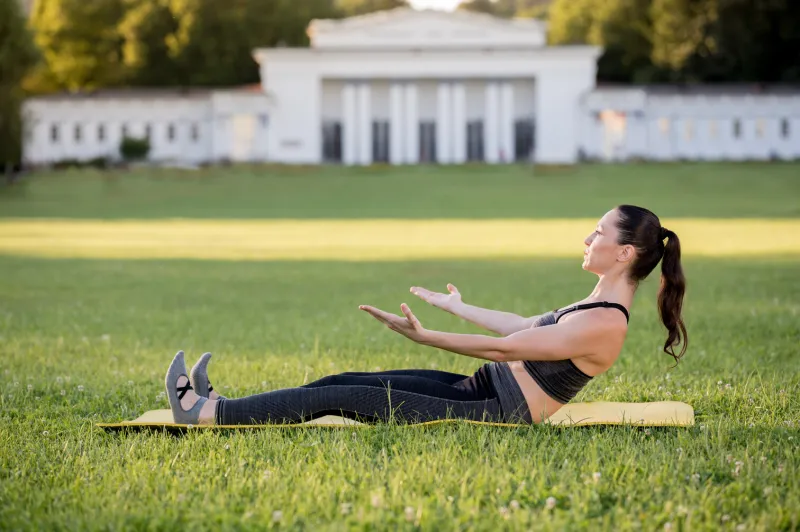 beautiful young woman lying on a yellow mattress, pose while wearing a tight sports outfit in the park doing pilates or yoga, roll up intermediate exercises