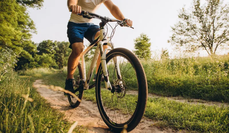 a man rides a bicycle on a dirt road in the summer at sunset active rest in the summer on bicycles cycling between the fields in the summer at sunset