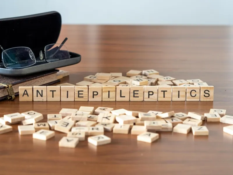 antiepileptics concept represented by wooden letter tiles on a wooden table with glasses and a book