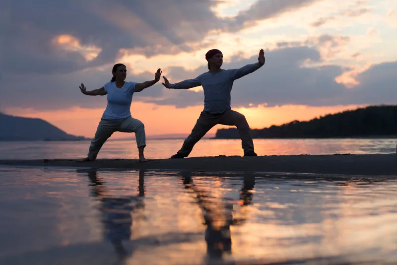 man and woman doing tai chi chuan at sunset on the beach solo