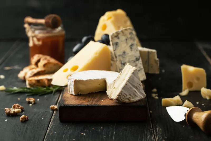 assorted cheeses with grapes, nuts and rosemary on a wooden background